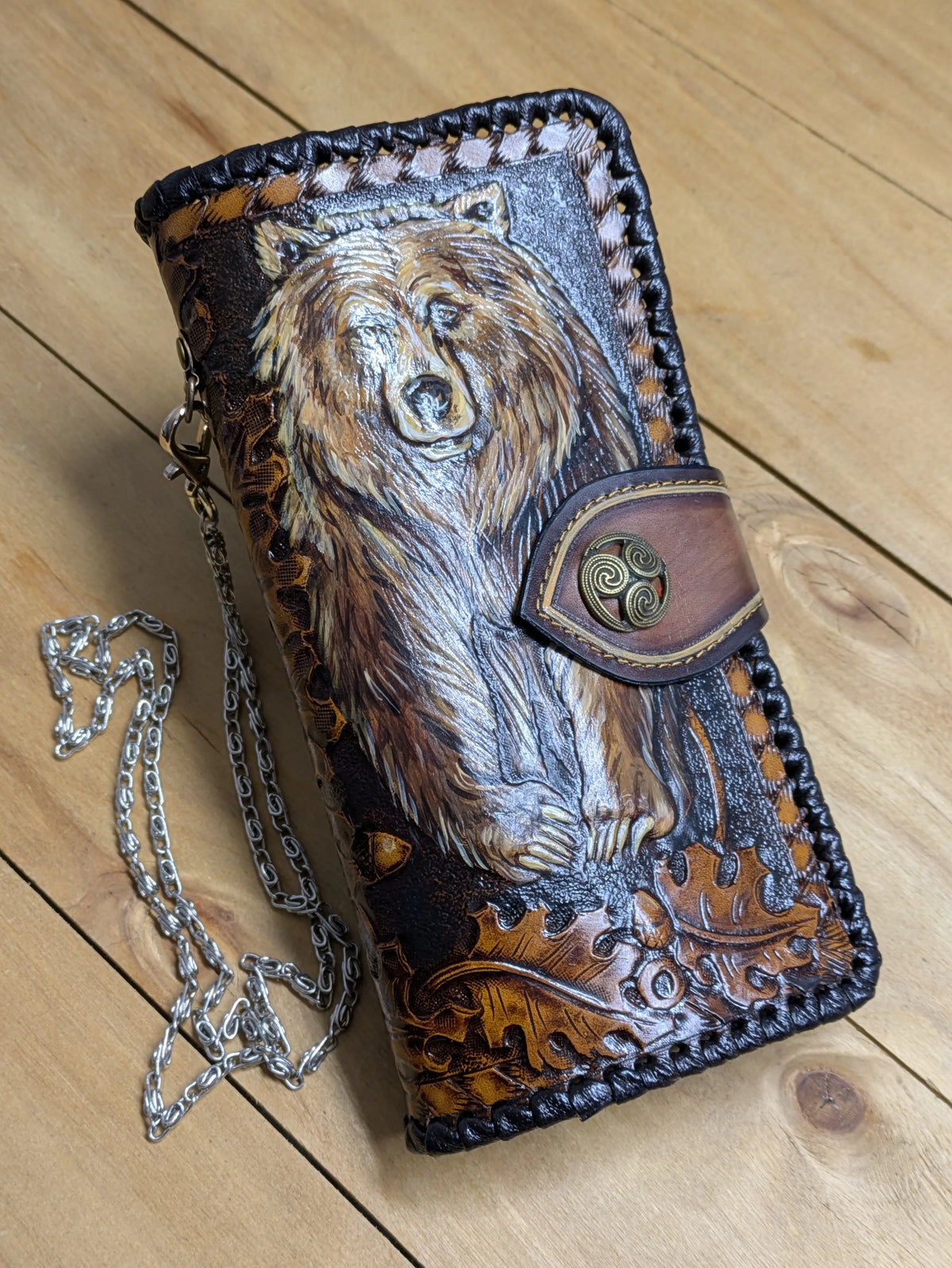 Top-down view of a hand-painted brown grizzly bear biker wallet with a silver chain on a light wood background.