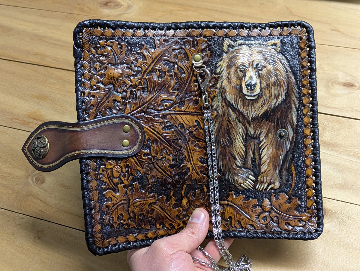 Full layout of an open leather truck wallet showing detailed oak leaf tooling alongside a hand-carved grizzly bear.
