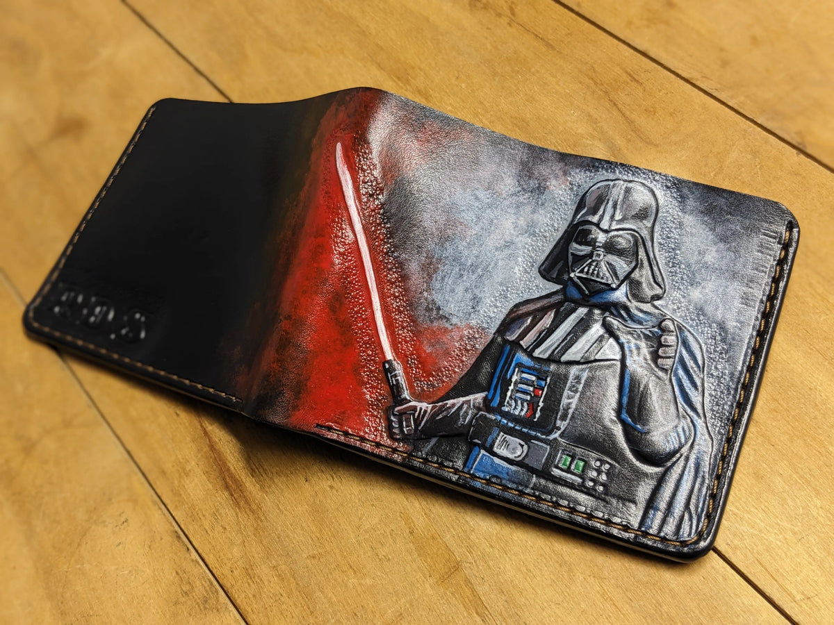 Open hand-tooled leather wallet with a detailed carving of Darth Vader and a vibrant red lightsaber glow effect.