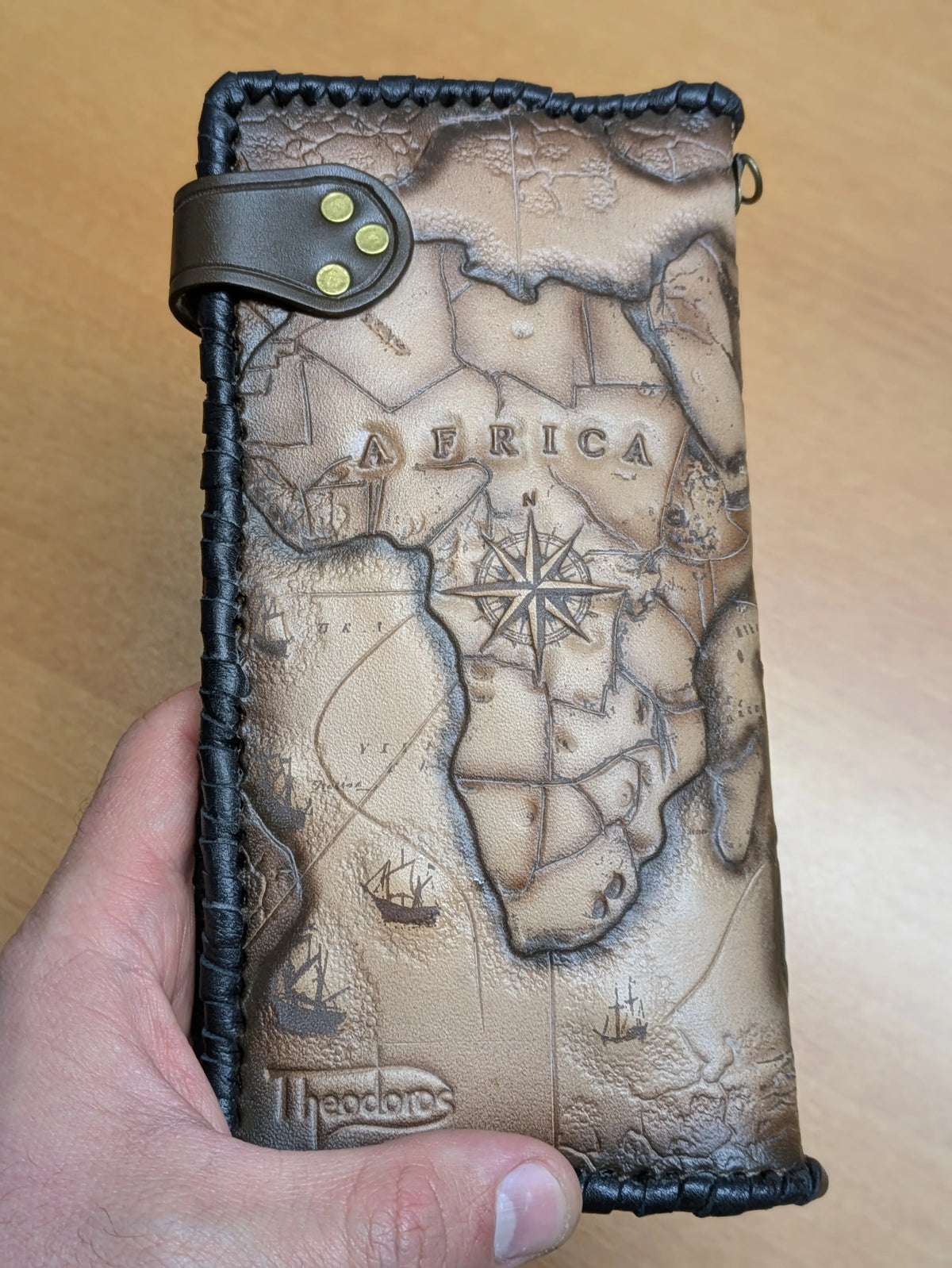 Theodoros Leather travel wallet back cover featuring a hand-tooled Africa map, nautical compass, and stamped brand logo.