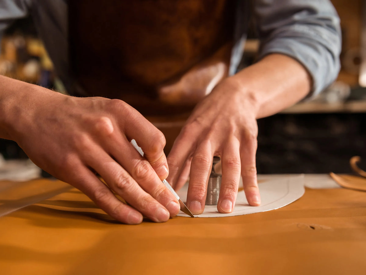 Close-up of artisan hands precision-cutting custom leather patterns for high-end wallets in the Theodoros leathercraft studio.