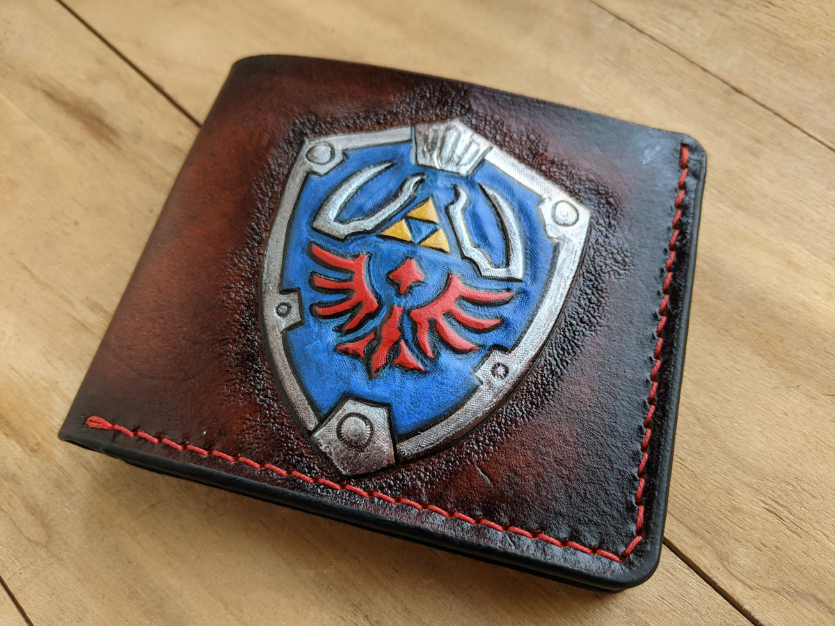 Close-up view of a custom painted Hylian Shield hand-tooled on a full-grain leather LOZ wallet, crafted by Theodoros Leather.