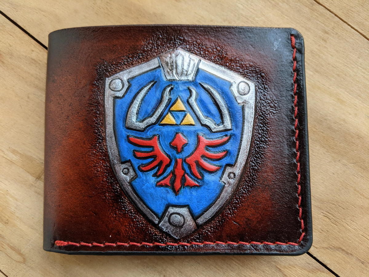 Hand-tooled full-grain leather Zelda wallet showing the detailed Triforce and Crest of Hyrule emblem, custom-made by Theodoros.