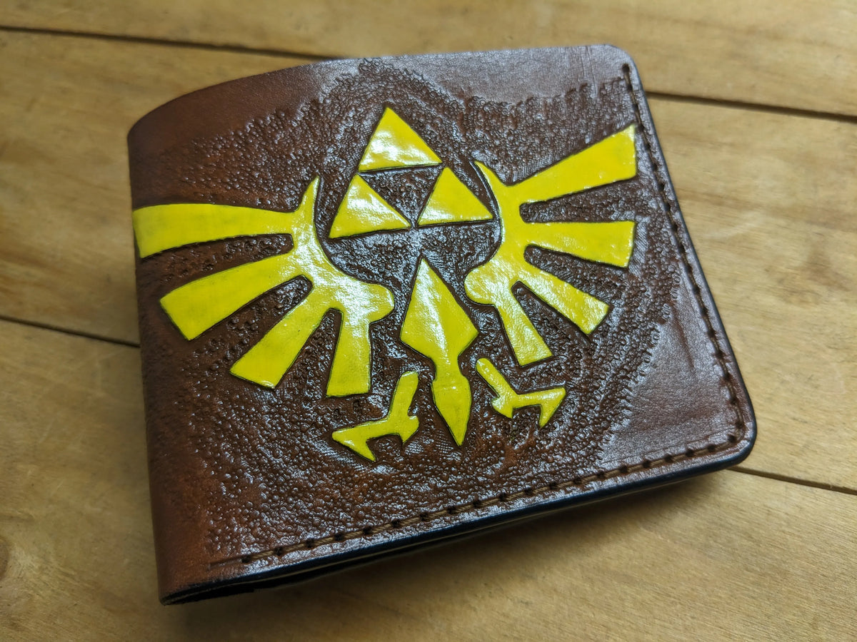 Close-up of a handmade full-grain leather Zelda wallet featuring an embossed Hylian Crest with precise gold paint detailing.