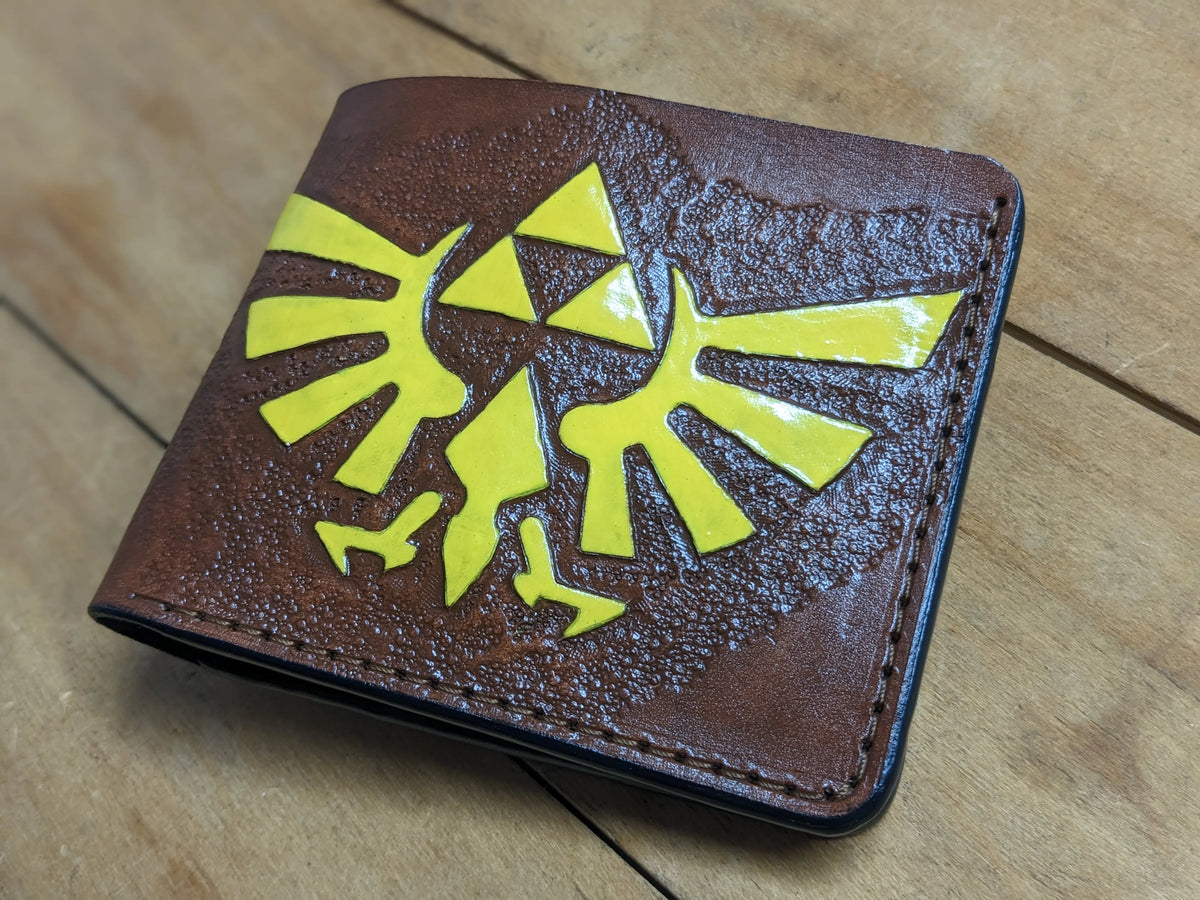 Custom Legend of Zelda full-grain leather bifold wallet showcasing the hand-carved gold metallic Triforce and Hylian Crest.
