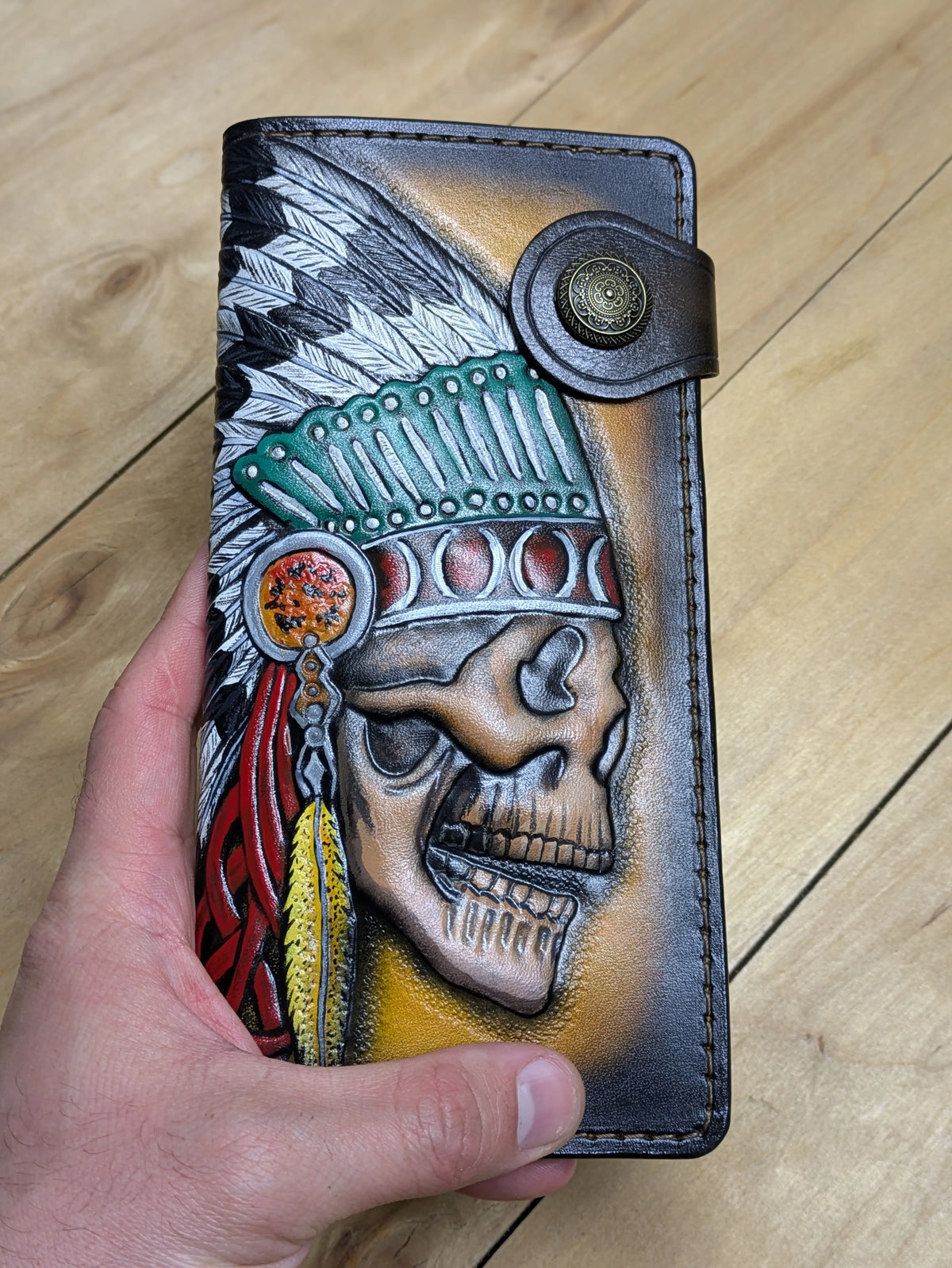 Close-up of the front of a hand-carved leather long wallet, highlighting the high-relief texture of the Indian skull.
