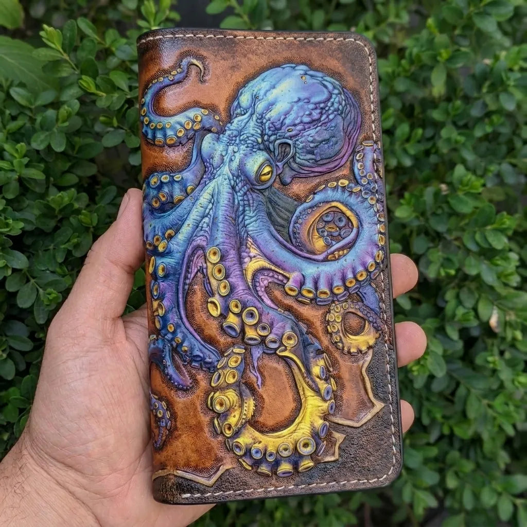 Close-up of a hand holding a long, hand-painted leather truck wallet featuring a detailed blue sea monster octopus.