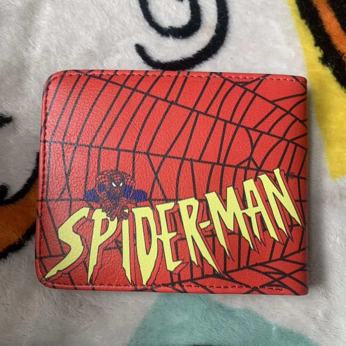 Back view of a red bifold leather wallet featuring the classic yellow and green Spider Man comic book typography logo over webs.