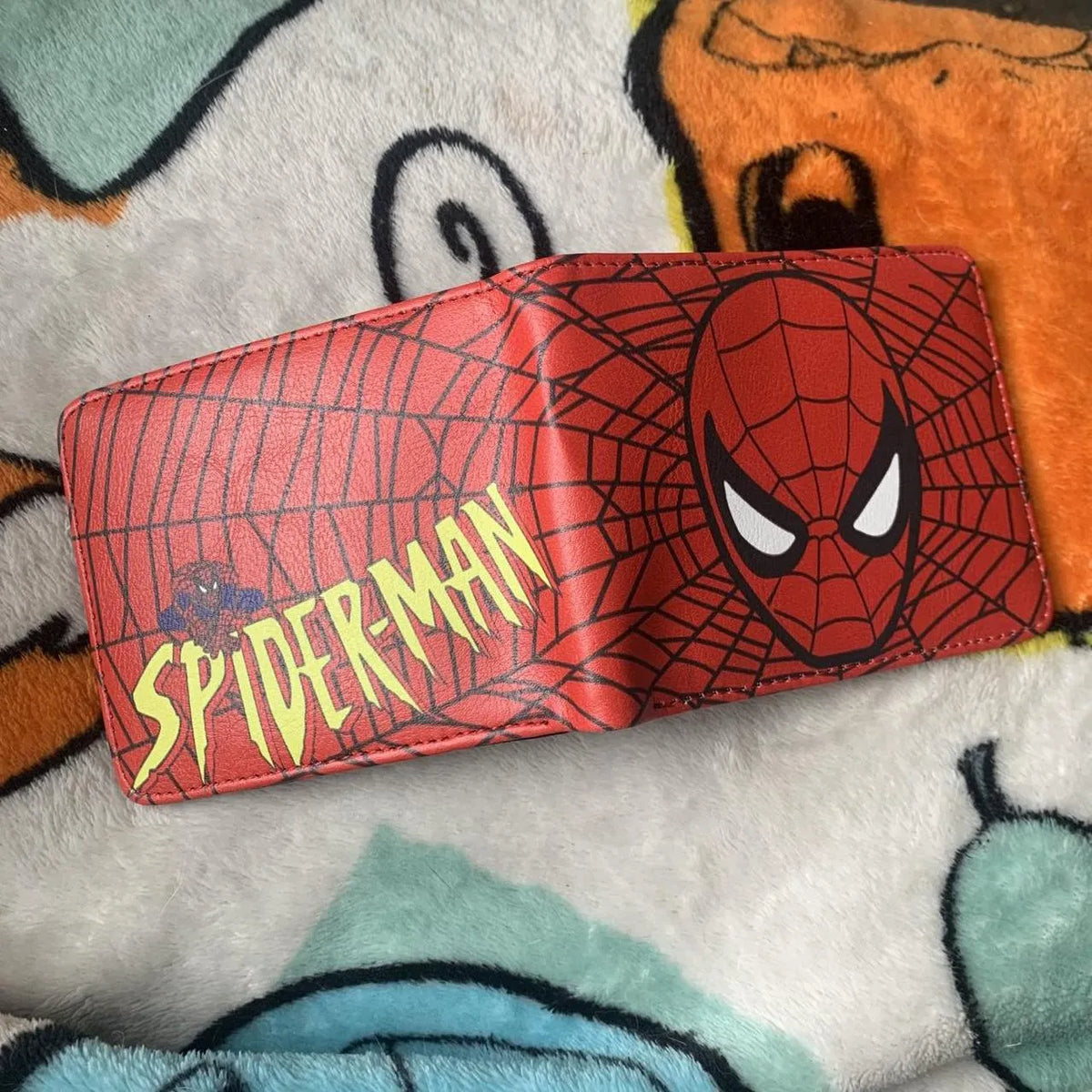 Fully opened red Spider Man leather wallet showing the mask graphic on the front and the yellow vintage comic logo on the back.