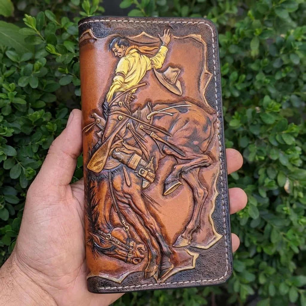 Handheld close-up of a long leather truck wallet with a detailed, hand-painted cowboy and bucking horse design.